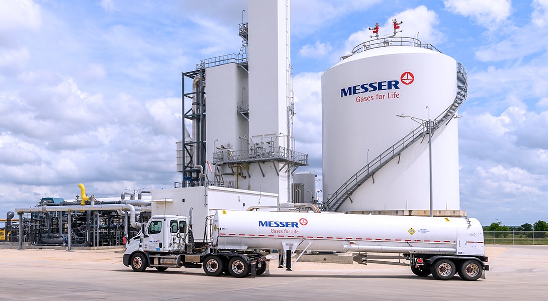Messer tanker truck parked in front of a large industrial gas storage tank and production facility.