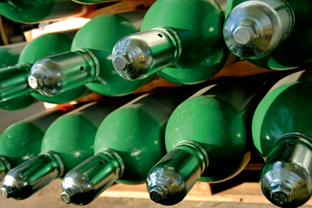 Close-up of green compressed-gas cylinders stored horizontally in a rack, with metal valve caps facing outward.