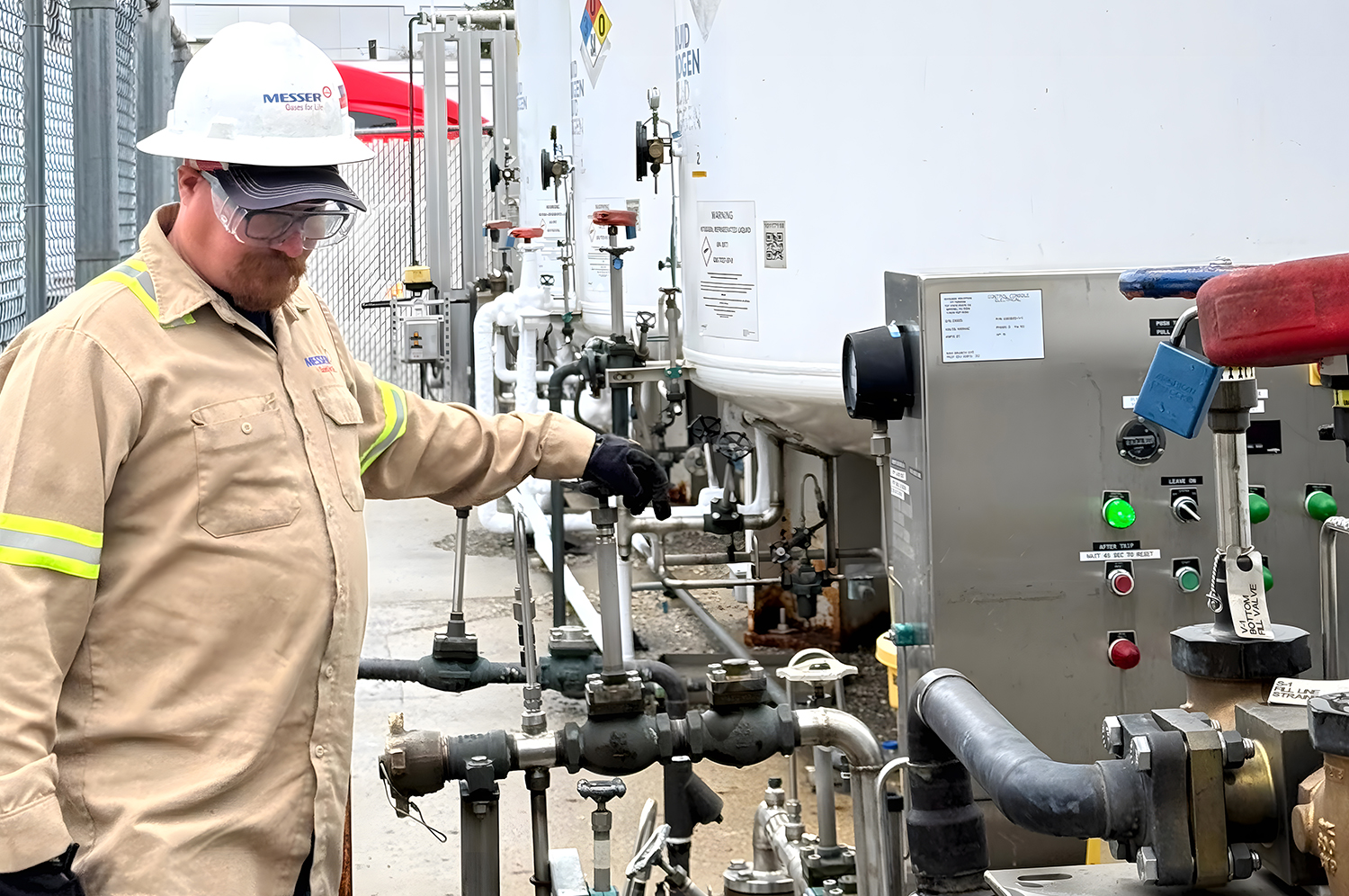 A Messer technician wearing PPE inspects valves and control equipment at a bulk liquid gas storage tank during a routine safety check.