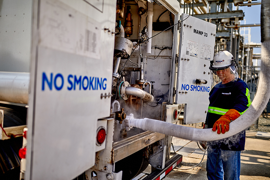 Messer worker wearing protective equipment handles a transfer hose while servicing industrial gas.